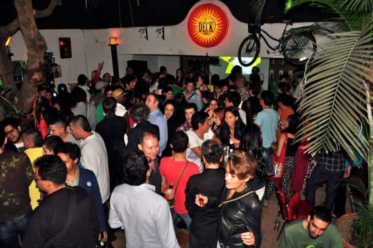 Bar and nightclub scene with a large crowd, live music, neon signs, and tropical decor at Eventario, emphasizing event planning, social gatherings, and nightlife organization in Colombia.