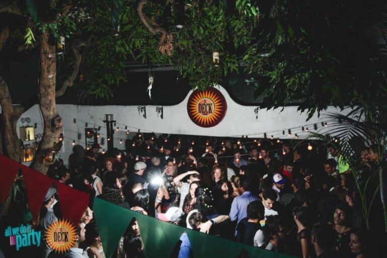 Deck event en fiesta al aire libre, congregando jóvenes en un ambiente de diversión, música y socialización bajo luces y árboles. Evento ideal para promover experiencias únicas y dinámicas.