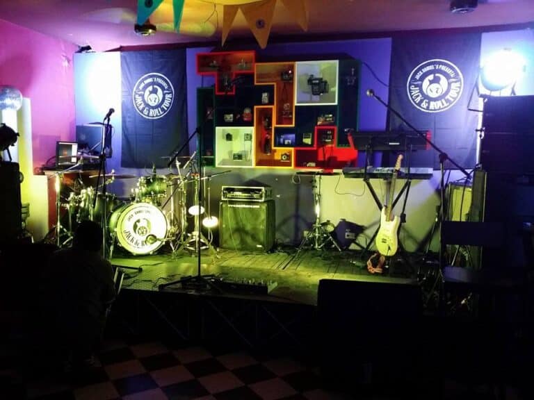 Banda musical en escenario decorado con luces y instrumentos en un espacio de evento con ambiente vibrante y colorido.