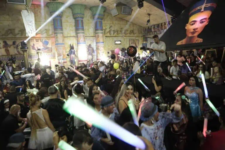 A crowded party with colorful lights and music in a vibrant, lively atmosphere at an Egyptian-themed venue with artistic decor.