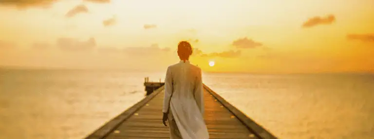 夕阳西下，海面上的木桥上，一位女子在金色的天空和夕阳的映衬下漫步，为各种活动和体验增添色彩。