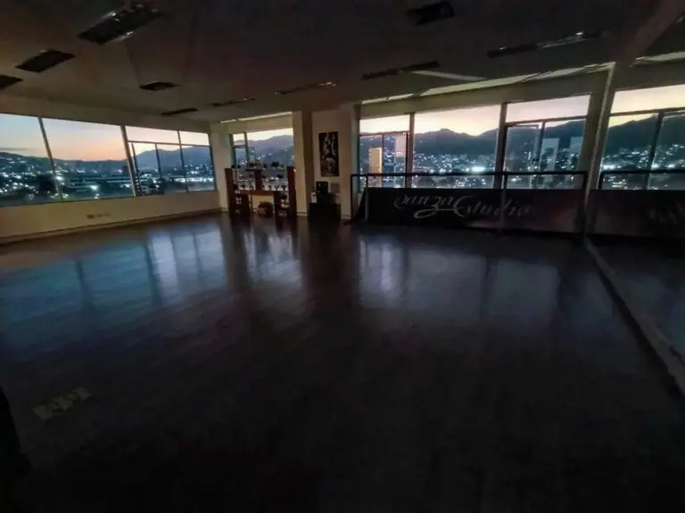 Ampia sala eventi con vista panoramica sulla città e sulle montagne al tramonto, ideale per riunioni e celebrazioni in un ambiente elegante e moderno.
