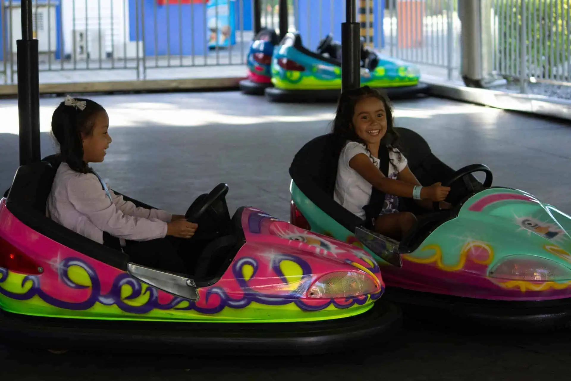 Mädchen genießen Fahrten auf Karnevalswagen auf einem Kinderjahrmarkt. Nahaufnahme glücklicher Mädchen in einem Vergnügungspark mit Kinderfahrgeschäften.