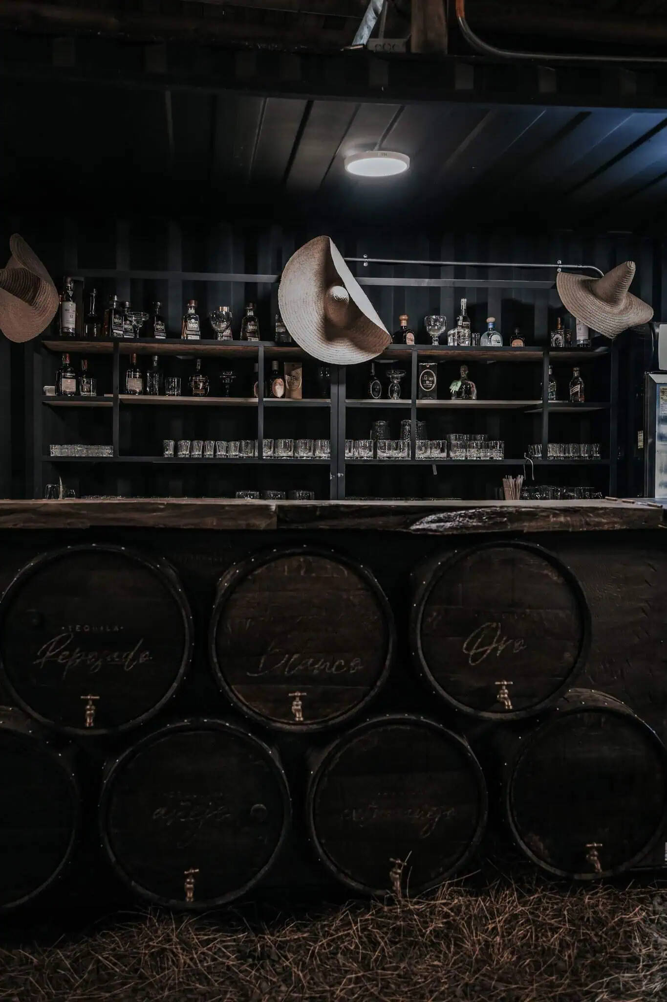 Un bar de style rustique avec des fûts de tequila et des chapeaux de paille, idéal pour les événements et les célébrations, avec une atmosphère chaleureuse et accueillante pour s'amuser et passer de bons moments.