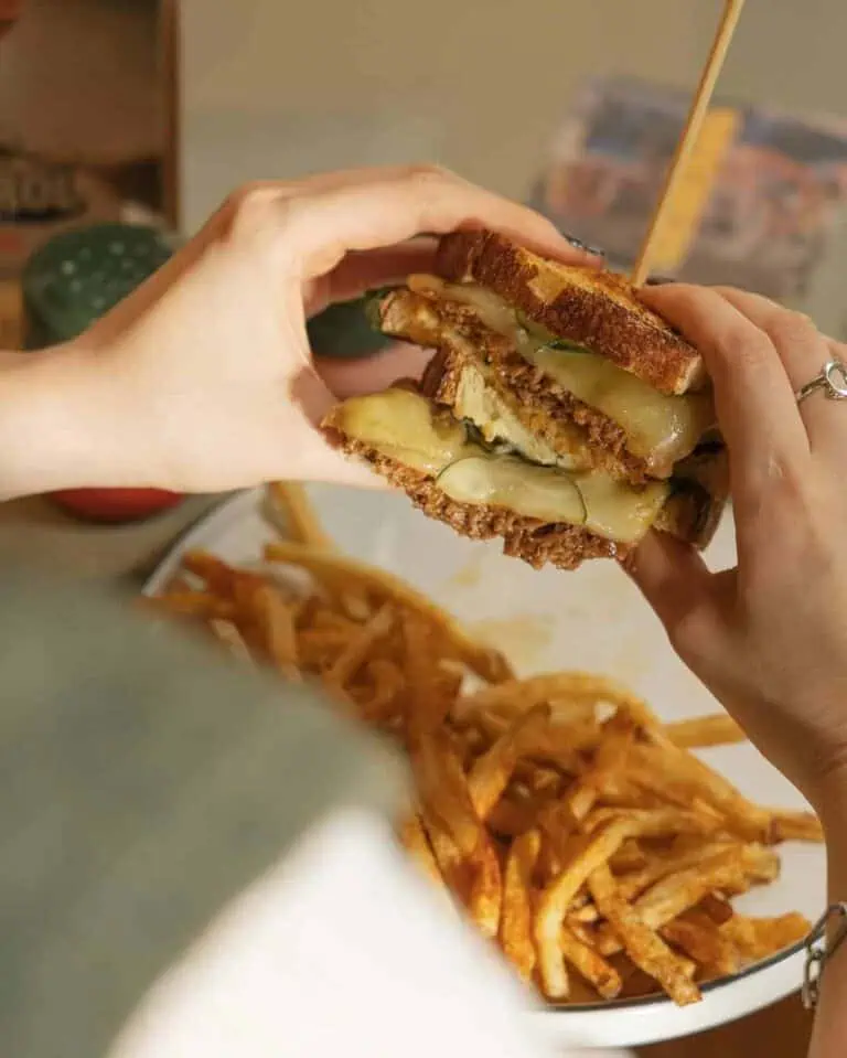 Un sandwich cheeseburger au bœuf et au pain grillé, à la main, avec des frites croustillantes au fond, une nourriture rapide et délicieuse dans un style décontracté.