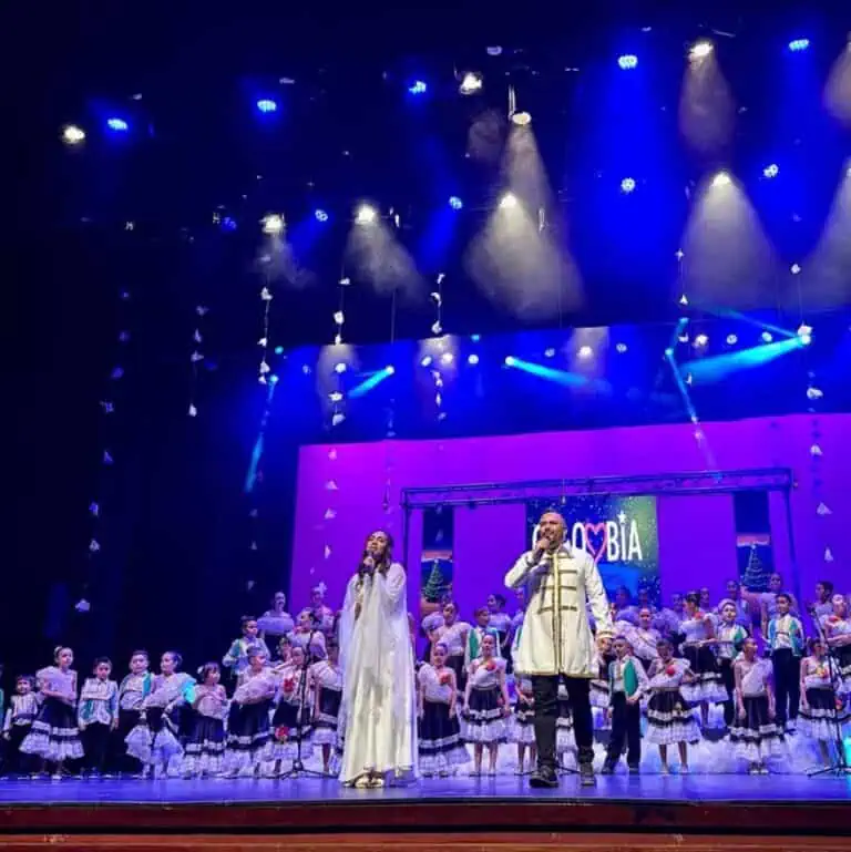 在一次文化艺术活动中，一男一女与身着哥伦比亚传统服饰的孩子们一起在舞台上唱歌。