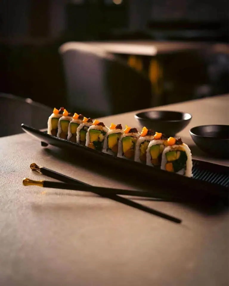 黑色盘子上摆放着切得非常紧实的寿司，前景是日式筷子，背景是黑色碗，风格优雅简约，适合哥伦比亚的活动和餐饮服务。