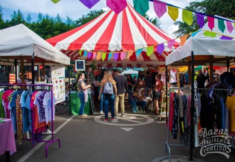Colorful stalls at a craft and clothing fair at an outdoor event with pennant decorations on a sunny day.