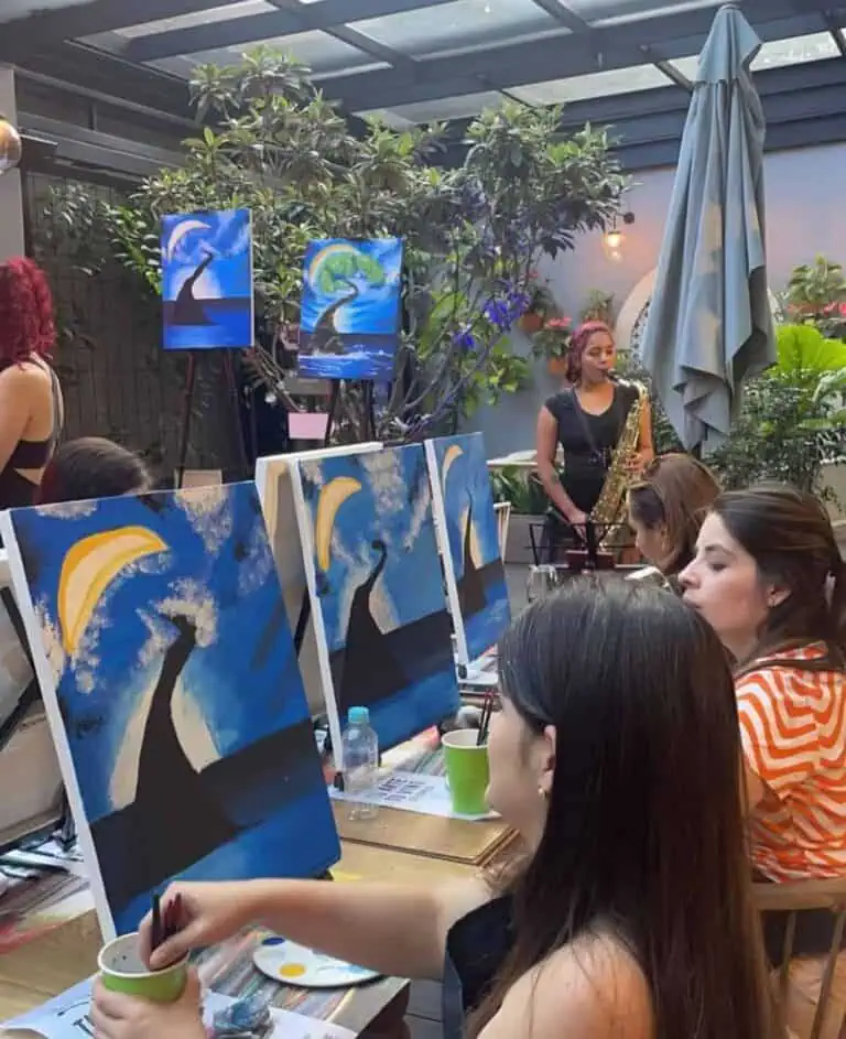 Peinture en direct lors d'un événement artistique avec des artistes et le public appréciant l'art dans un espace avec de la végétation et des œuvres d'art inspirées de la mer et de la nature.