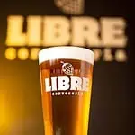 一杯印有 LIBRE 啤酒厂标志的精酿啤酒，背景是 LIBRE 的标志和一个泡沫丰富的啤酒锥。