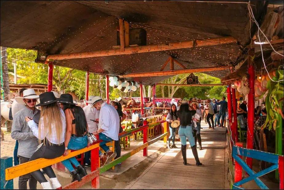 Groupe de personnes lors d'une foire ou d'un événement en plein air avec des décorations festives et de la musique live dans une atmosphère colorée et familiale en Colombie.
