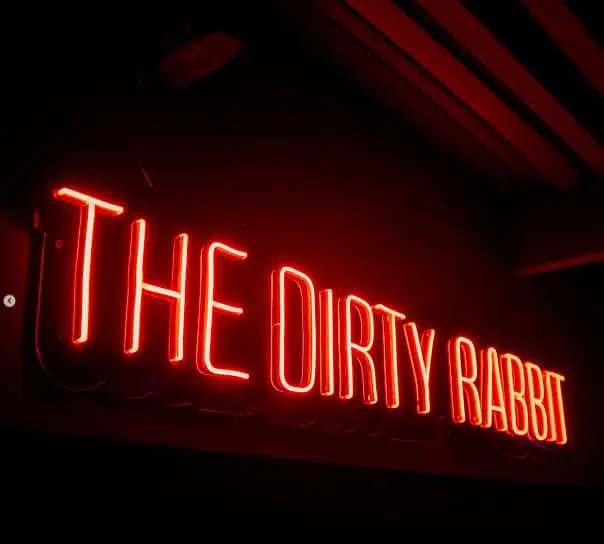 在昏暗的环境中，红色霓虹灯招牌上写着“脏兔子”，是波哥大夜间活动和体验的理想场所。