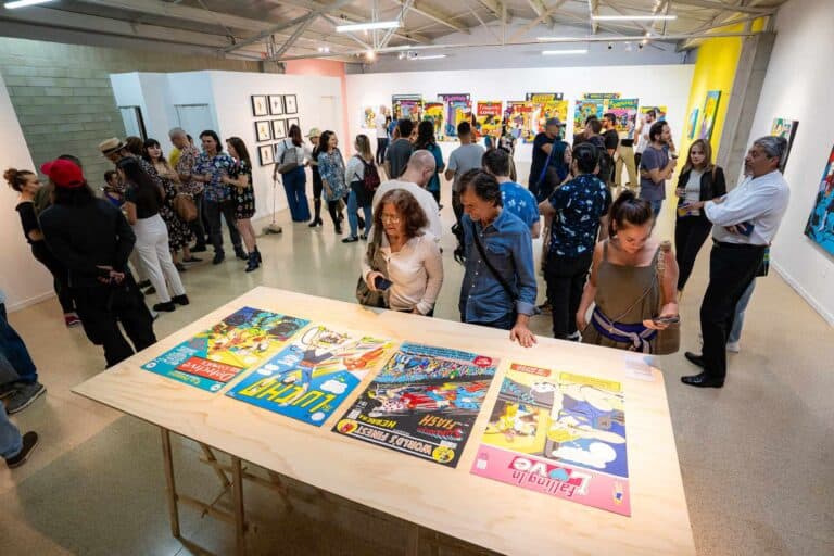 Disfruta en una exposición de arte en Bogotá, donde asistentes admiran cómics y obras de arte modernas en un ambiente cultural y vibrante, promoviendo el arte y la creatividad.