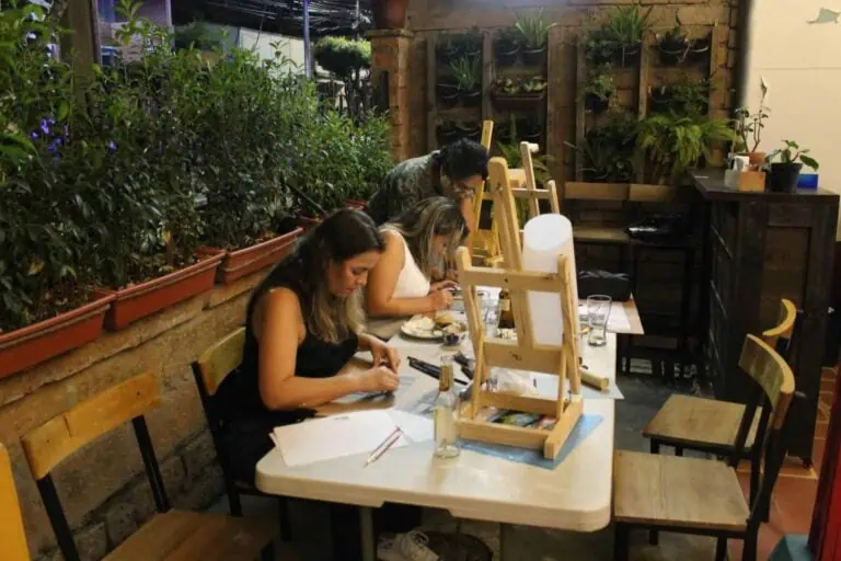 Kreative in einem Mal- und Kunstwerkstatt in einem Innenraum mit Pflanzen und rustikalem Dekor. Menschen, die in einem gemütlichen und modernen Ambiente an einer künstlerischen Aktivität teilnehmen.
