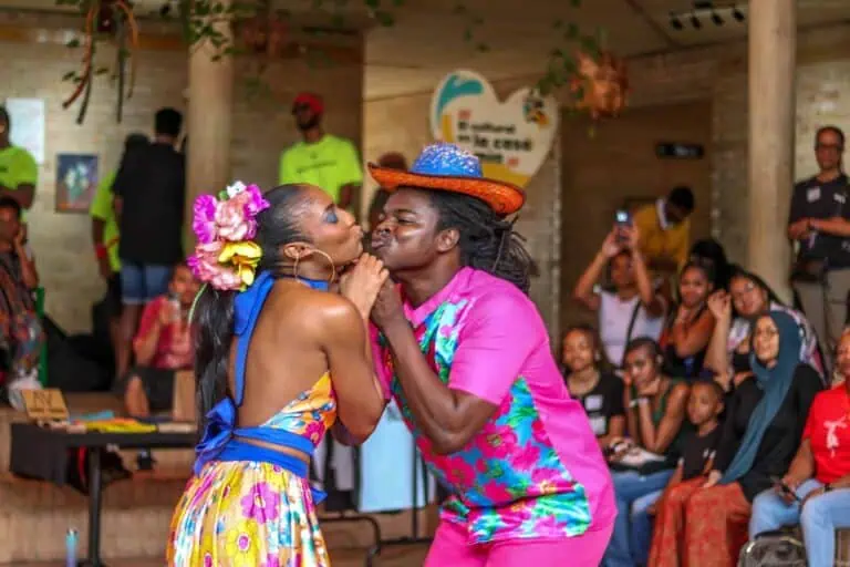 Un couple dynamique dansant et s'amusant lors d'un événement culturel colombien, vêtu de costumes traditionnels et d'accessoires colorés, entouré d'un public et d'une ambiance festive à l'intérieur.