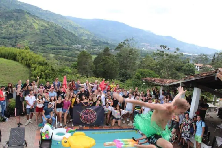 Fiesta al aire libre con grupo diverso de personas disfrutando evento en naturaleza, piscina y decoraciones coloridas, en un entorno montañoso facilitar coordinar eventos y reuniones en espacios únicos y naturales en Colombia.