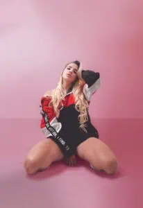 Jeune fille posant dans un studio avec un fond rose, portant des vêtements de sport modernes, un style urbain et une attitude confiante, idéale pour la promotion d'événements et la mode urbaine en Colombie.