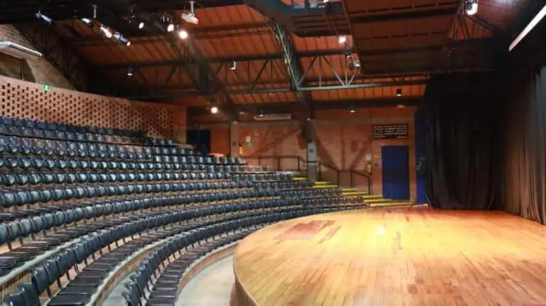 Posti a sedere a teatro in uno spazio per eventi culturali con palco in legno e illuminazione mirata, ideale per presentazioni, rappresentazioni teatrali e spettacoli a Bogotà.