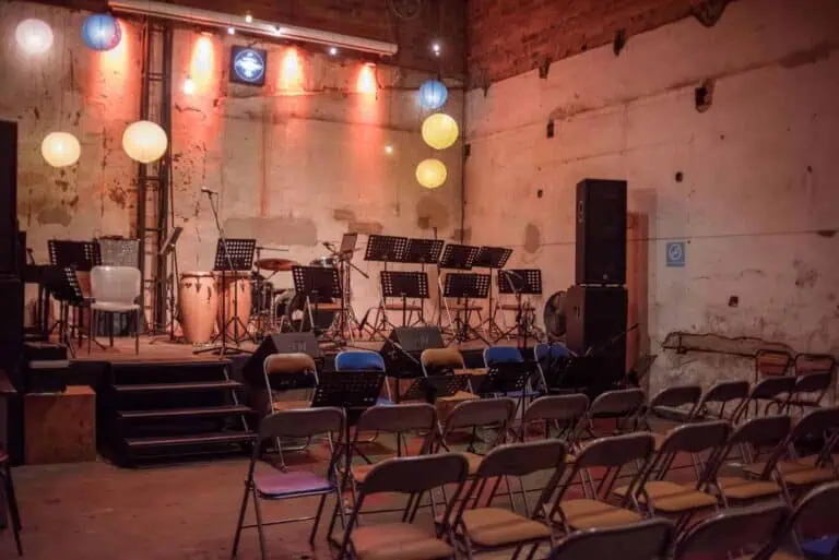 Eine Eventbühne mit Ambientebeleuchtung, Musikinstrumenten und Sitzgelegenheiten für Konzerte oder Präsentationen in einem Innenraum mit Backsteinwänden.