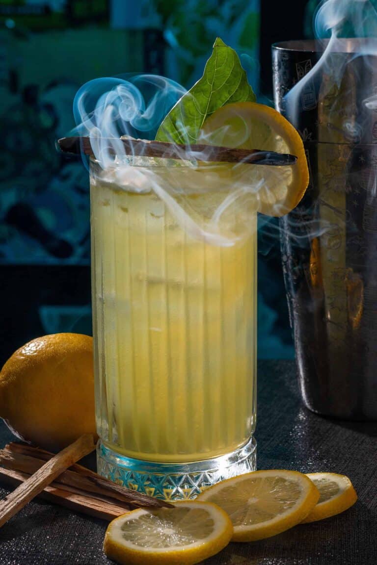 Refrescante cóctel de limón con hielo y hojas de menta, decorado con una rodaja de limón, en un escenario oscuro con ingredientes y accesorios de bar. Perfecto para eventos y coctelería en Colombia.