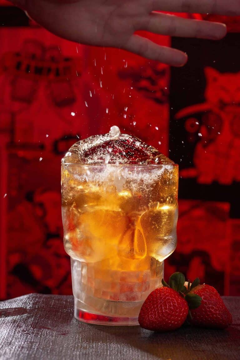 Refresco con hielo y limón en vaso de vidrio, fresas en primer plano, fondo rojo, ambiente festivo, evento, cocktail, bebida refrescante, celebración, imagen de evento, promoción de eventos, evento corporativo, cocktail party.