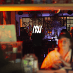 DJ en un evento en vivo en un restaurante o bar nocturno con ambiente vibrante y luces de neón, promoviendo servicios de eventos y entretenimiento en Colombia.