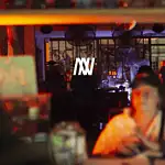 DJ lors d'un événement en direct dans un restaurant ou une boîte de nuit avec une atmosphère vibrante et des néons, faisant la promotion de services d'événements et de divertissement en Colombie.