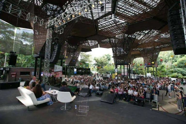 Un auditorium en plein air pour un événement de conférence avec une structure en bois et une scène, entouré de nature et d'un public.