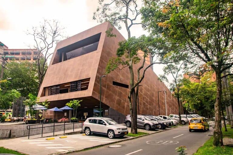 Modern building in city park with parking lot and trees, urban architecture, innovative design for event spaces, sustainable construction, eco-friendly facilities, modern event infrastructure, urban development, architectural innovation.