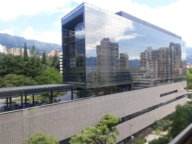 现代化的办公楼，拥有玻璃幕墙，可以映照出城市和附近山脉的景色，坐落在绿树环绕的城市环境中。