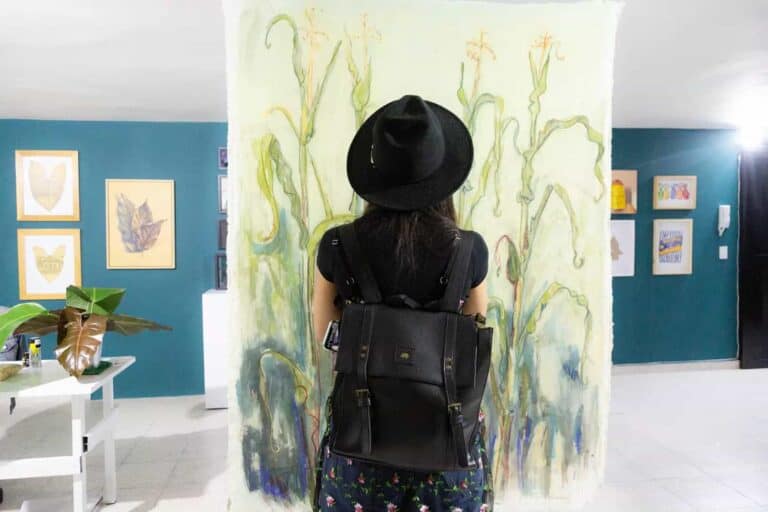 Fotografía de una mujer observando obra de arte en galería de exposición, con fondo de paredes decoradas, enfocada en creatividad e inspiración artística en eventos culturales.