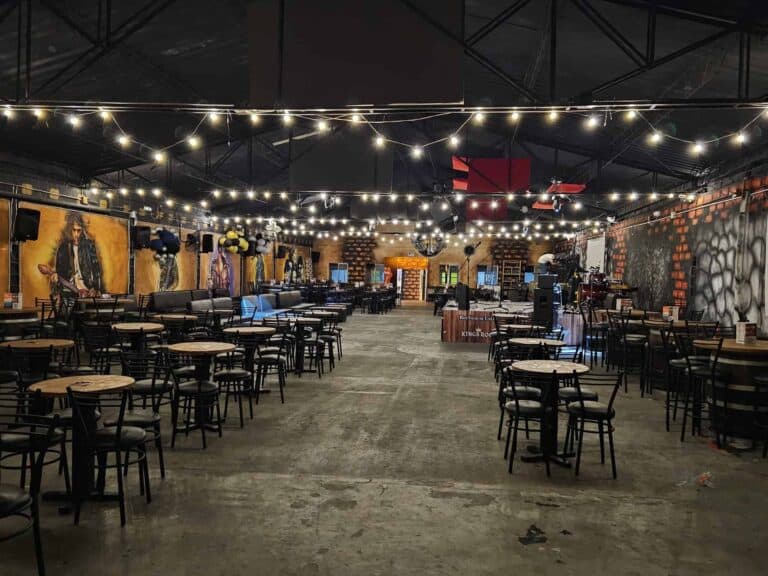 Sala de eventos iluminada con luces decorativas, mesas y sillas de madera, ideal para conciertos, fiestas o reuniones sociales en un ambiente moderno y acogedor.