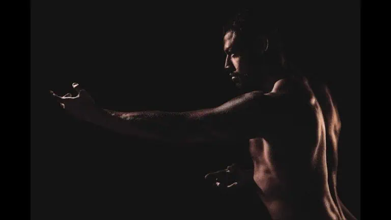 Homme athlétique en mouvement dans une faible lumière, mettant en évidence les muscles et la posture sur un fond noir.