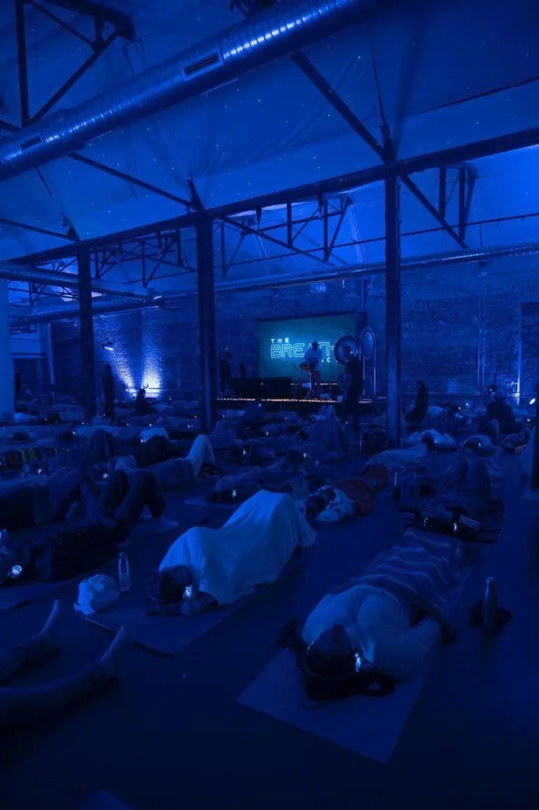 Un groupe de personnes participant à un cours de yoga en soirée dans un espace industriel avec un éclairage bleu et une technologie moderne, promouvant le bien-être et la pleine conscience lors d'événements d'entreprise.