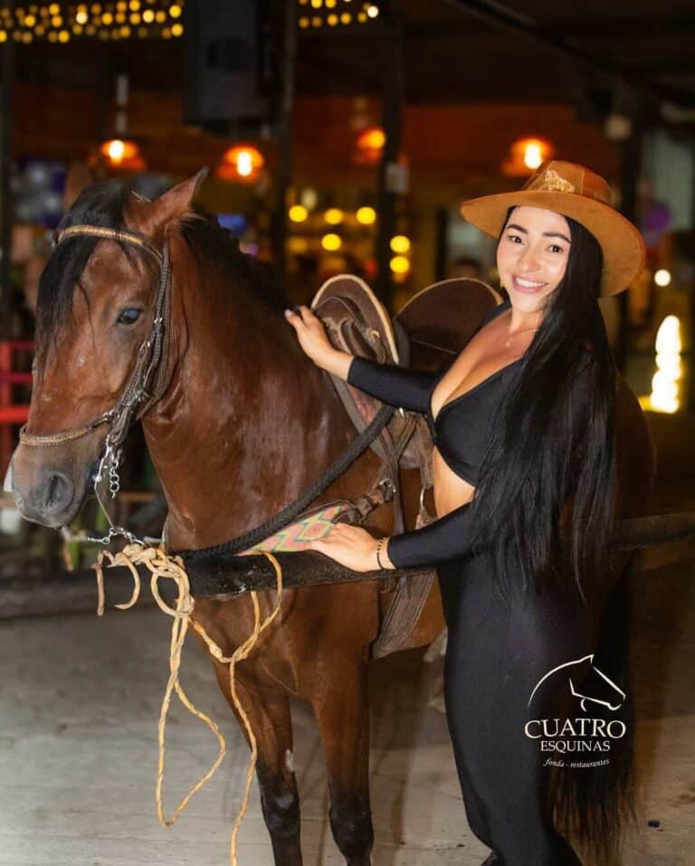 Caballo de carreras en ambiente nocturno con mujer vestida con estilo rústico y sombrero de paja, en evento o espectáculo ecuestre en un lugar con iluminación cálida y decoraciones temáticas.