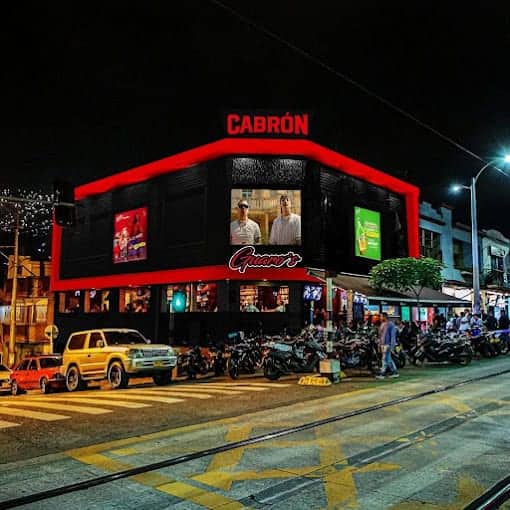 Cabron, edificio con pantallas digitales y motos estacionadas, iluminación nocturna, ambiente urbano y comercial, fotografía de negocio y tecnología, evento y publicidad, en clima nocturno urbano en Colombia.