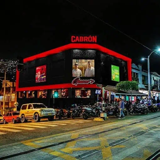 Cabron, a building with digital screens and parked motorcycles, nighttime lighting, urban and commercial atmosphere, business and technology photography, event and advertising, in an urban nighttime setting in Colombia.