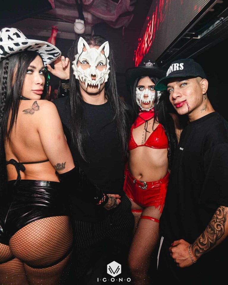 Disfraces de Halloween con máscaras de fantasmas, vampiros y calaveras en un evento temático en Bogotá. Personas vestidas con ropa atrevida y accesorios que reflejan un ambiente festivo y de disfraces.