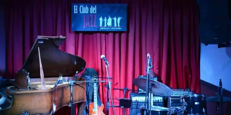 在哥伦比亚麦德林的一家爵士俱乐部里，钢琴、鼓和麦克风摆放在舞台上，准备进行一场现场音乐会。舞台上挂着红色幕布，还有一块牌子宣传着这场音乐活动。