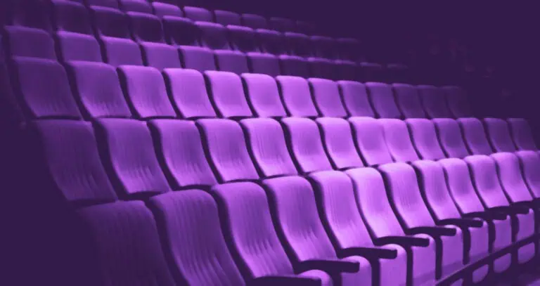 Rows of pink chairs in a dark auditorium, ideal for events and conferences with an elegant and modern atmosphere.