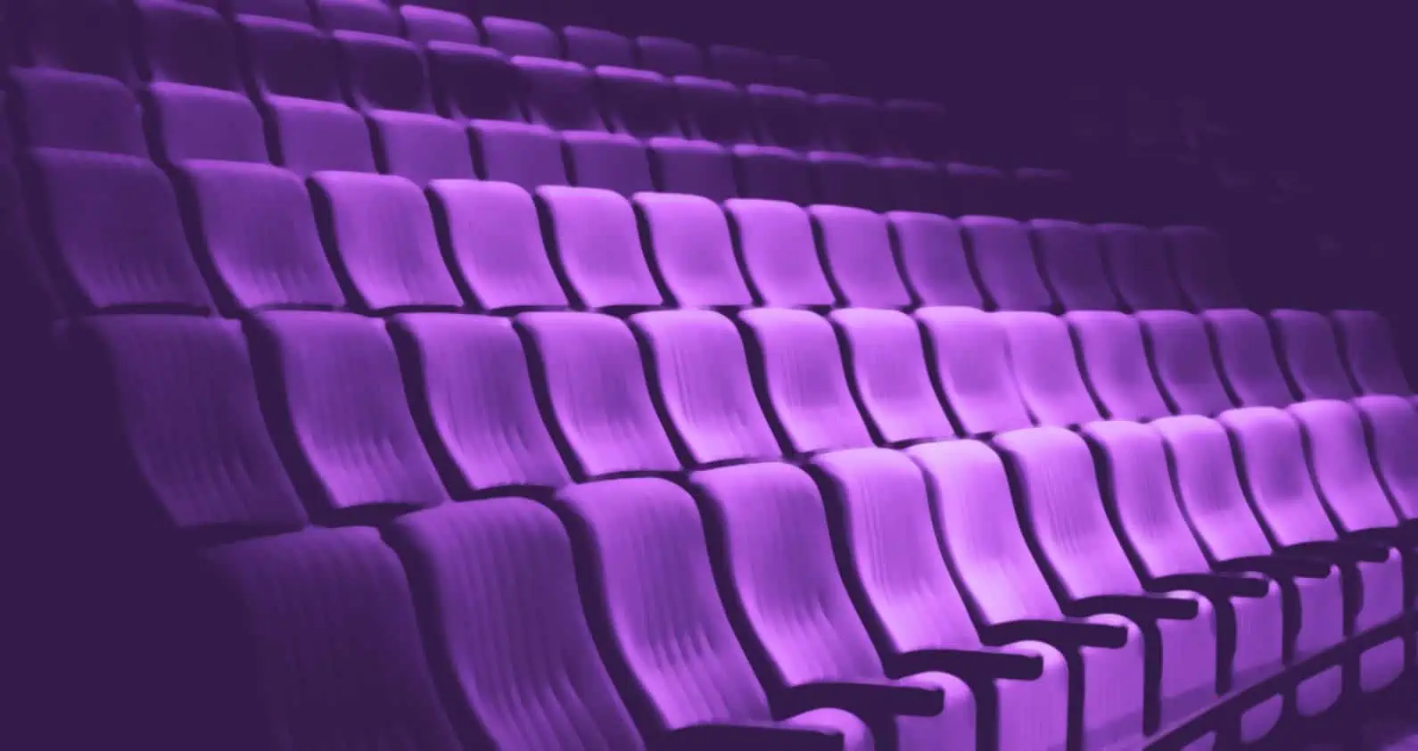 Rows of pink chairs in a dark auditorium, ideal for events and conferences with an elegant and modern atmosphere.