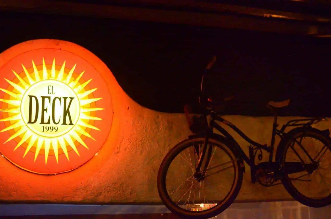 在昏暗的环境中，墙上悬挂着白色和黄色的“El Deck 1999”字样的发光信笺，背景中有一辆自行车，非常适合在卡塔赫纳宣传活动和餐厅。