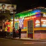 色彩缤纷的建筑物装饰着灯光和街头活动海报，人们在夜色中社交，气球飘扬。