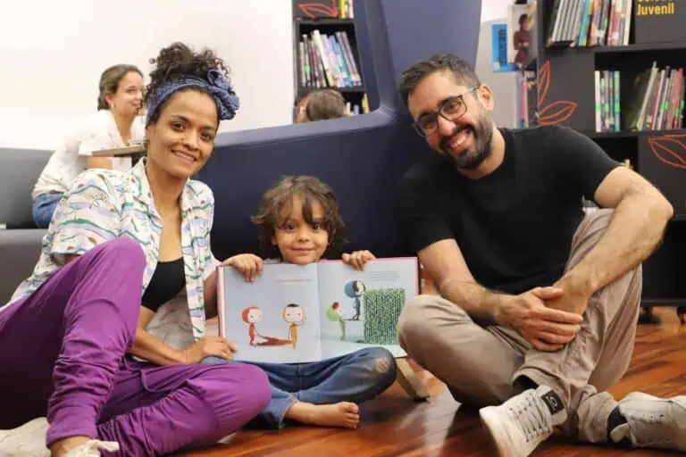 Une fille lit un livre pour enfants avec des adultes dans une bibliothèque, faisant la promotion d'événements culturels pour les enfants.