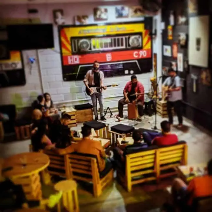 一支乐队在私密空间里为活动演奏，观众坐在木椅上，气氛温馨，装饰复古，是波哥大举办活动和音乐会的理想场所。