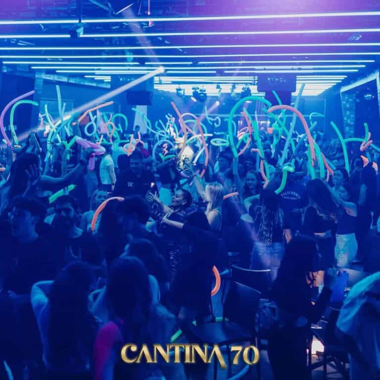 Fiesta en Cantina 70 con música en vivo y luces de neón, ambiente vibrante y energía alta en un evento social con muchas personas bailando y disfrutando de la noche.