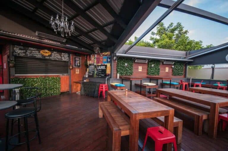 Moderno espacio de eventos al aire libre en un restaurante con mobiliario de madera, decoración verde y ambiente acogedor para reuniones y celebraciones en Colombia.