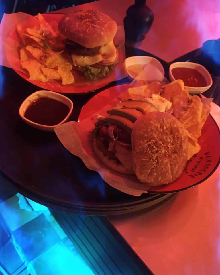 Burgers y alimentos en un restaurante con iluminación de neón, presentación en platos con salsas y acompañamientos para eventos y reuniones sociales.