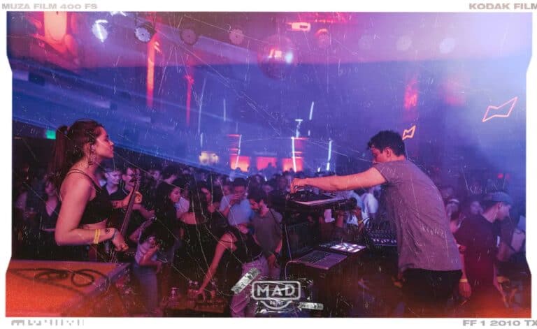 Audiencia en evento musical en un club con DJ en la cabina, ambiente de fiesta con luces y tecnología de audio profesional, imagen vibrante y enérgica para promoción de eventos y entretenimiento.