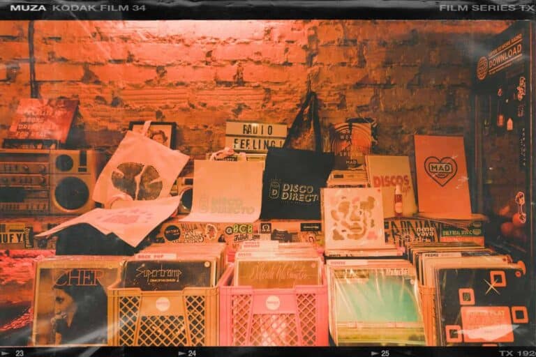 Discos de música y vinilos en display en una tienda o feria musical, con fondo de pared de ladrillo expuesto, ambiente vintage y colección de álbumes de diferentes géneros musicales.